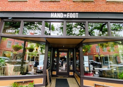 Entrance of a restaurant named "Hand + Foot," featuring large windows and a welcoming outdoor area.