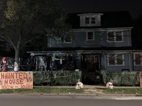 A spooky house decorated for Halloween, featuring skulls, a "Haunted House" sign, and eerie lighting at night.