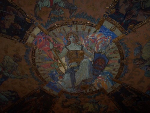 Ceiling mural featuring a central figure in armor, surrounded by colorful allegorical scenes and ornate decorations.