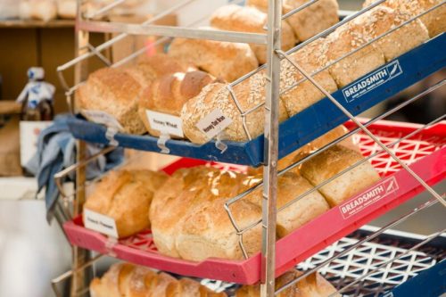 A display of various loaves of bread on metal racks, labeled with names like "Honey Wheat" and "Sourdough."