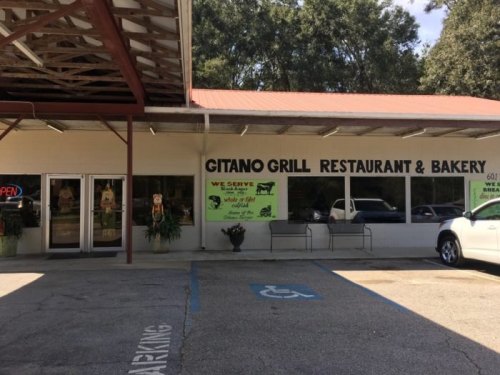 Exterior of Gitano Grill Restaurant & Bakery, featuring a sign and open windows, with a parking lot in front.