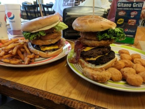 A towering burger with lettuce, onion rings, and cheese, served with fries and chicken nuggets on a colorful plate.