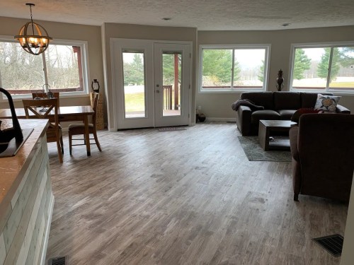 A spacious living area with large windows, a dining table, and a cozy seating arrangement, overlooking a green landscape.