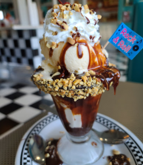 A delicious ice cream sundae topped with whipped cream, nuts, and chocolate sauce, served in a decorative glass.