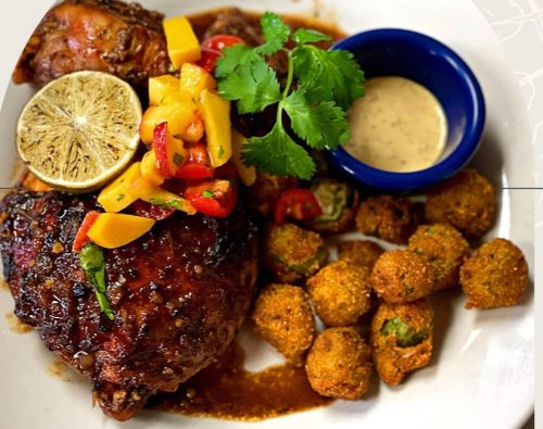 A plate featuring grilled chicken with mango salsa, lime, cilantro, and a side of fried okra and dipping sauce.