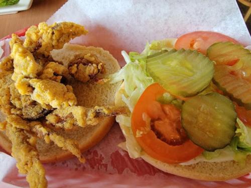 A sandwich with fried shrimp on one side and fresh lettuce, tomato, and pickles on the other, served on a bun.