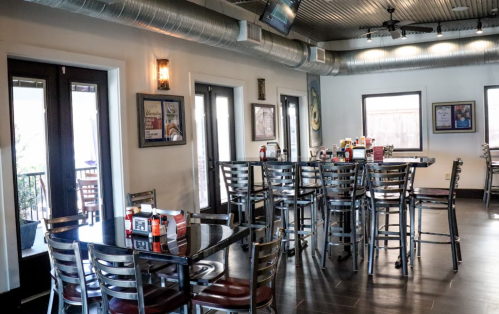 Interior of a restaurant featuring empty tables and chairs, with large windows and a modern decor.