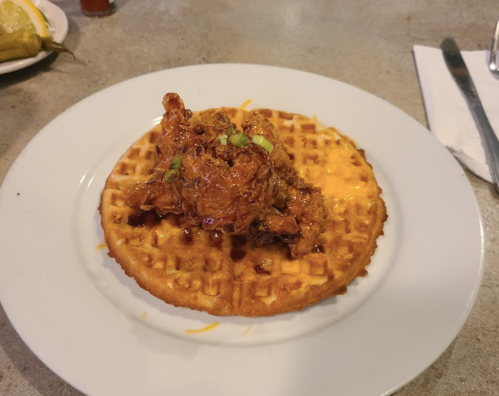 A plate featuring a golden waffle topped with crispy fried chicken and drizzled with syrup.