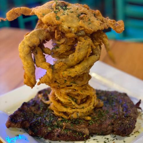 A juicy steak topped with a towering pile of crispy onion rings, garnished with herbs on a white plate.