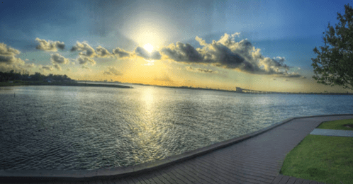 A serene waterfront view at sunset, with clouds and a vibrant sky reflecting on the water's surface.