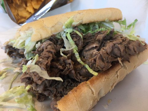 A close-up of a sandwich filled with shredded beef and lettuce on a soft hoagie roll.