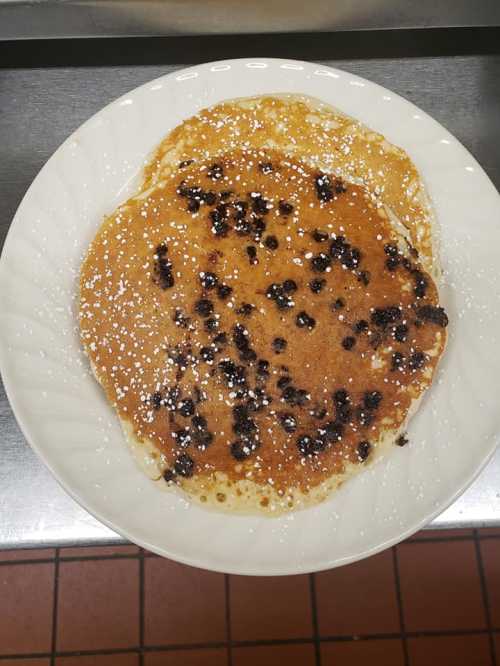 Two golden-brown pancakes topped with chocolate chips and dusted with powdered sugar on a white plate.