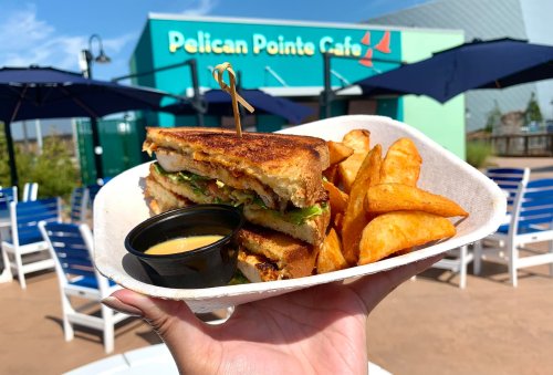 A hand holds a sandwich with lettuce and tomato, accompanied by golden potato wedges and a dipping sauce.