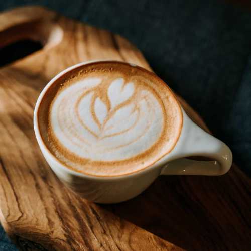 A latte with a leaf design in foam, served in a white cup on a wooden tray.