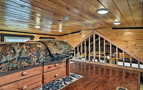 Cozy loft space with wooden walls, a bed with camouflage bedding, and a view of a staircase.