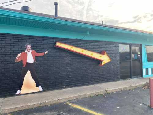 A colorful building exterior features a large arrow sign and a life-sized cutout of a person in a dance pose.