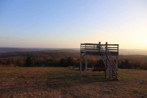 A wooden play structure with a slide and swings overlooks a scenic landscape at sunset.