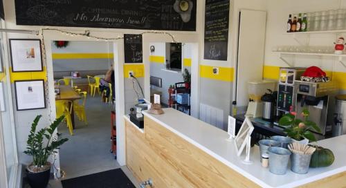 Bright café interior with a wooden counter, yellow accents, and seating area visible in the background.