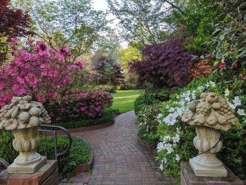 A serene garden path lined with vibrant flowers and greenery, flanked by decorative stone planters.