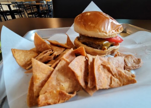 A burger with cheese and tomato on a bun, served with a side of crispy tortilla chips on a tray.
