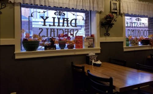 Cozy restaurant interior with wooden tables, decorative plants, and large windows featuring "Daily Specials" signs.