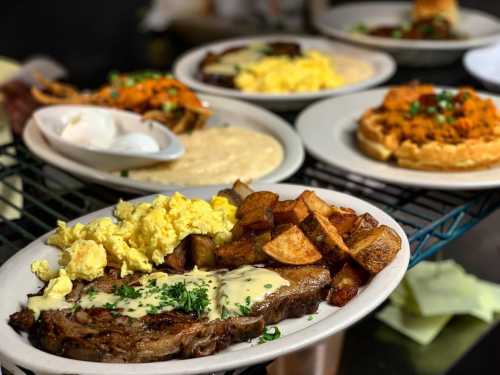 A plate of steak with scrambled eggs and potatoes, with other dishes in the background.