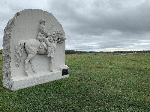 A stone monument of a soldier on horseback stands in a grassy field under a cloudy sky.