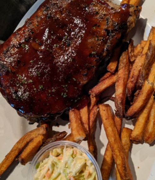 A plate featuring a glazed steak, crispy fries, and a small serving of coleslaw.