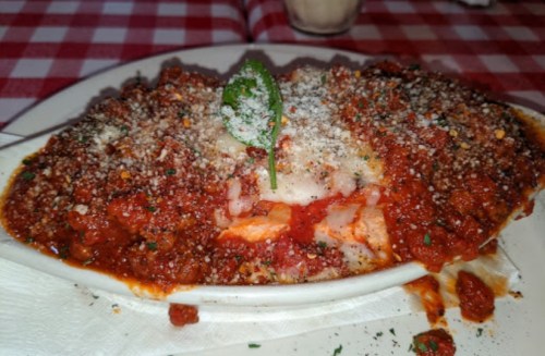 A dish of baked pasta topped with marinara sauce, cheese, and herbs, served on a white plate with a garnish.