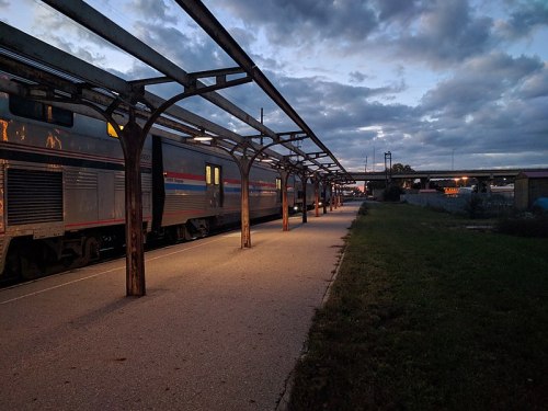 A train station platform at dusk, with empty tracks and cloudy skies overhead.
