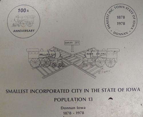 Illustration commemorating Donnan, Iowa, the smallest incorporated city, with trains and a 100th anniversary note.