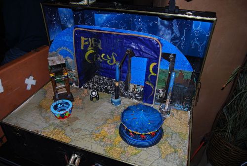 A creative diorama inside a suitcase, featuring a colorful stage with blue decorations and a map base.