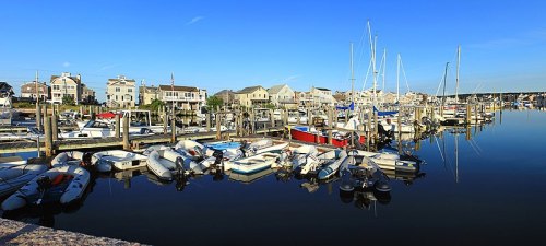 A serene marina with various boats docked, reflecting in calm water under a clear blue sky.