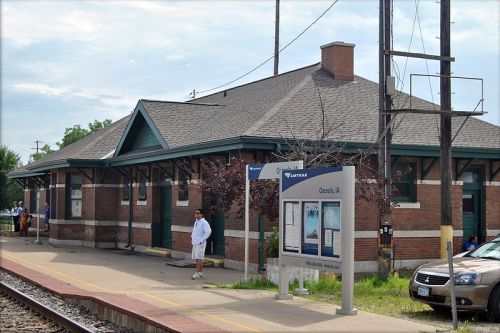A train station with a brick building, a waiting area, and a person standing on the platform.