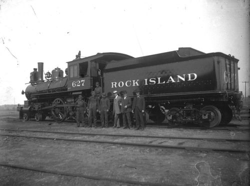 A historic steam locomotive labeled "Rock Island" with a group of men standing beside it on the tracks.
