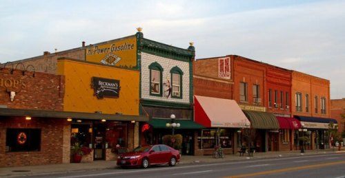 Colorful storefronts line a street, featuring vintage signage and awnings, with a car parked in front.