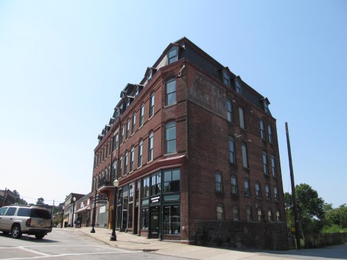 Historic brick building with multiple windows, angled view, clear blue sky, and a street in the foreground.