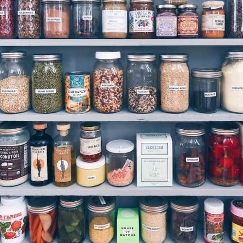 A neatly organized pantry shelf filled with various jars of grains, beans, spices, and canned goods.
