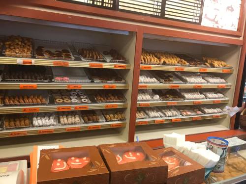 A display case filled with various baked goods, including cookies, pastries, and donuts, in a bakery setting.