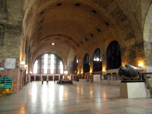 Interior of a spacious, historic train station featuring high arches, large windows, and a bison sculpture.