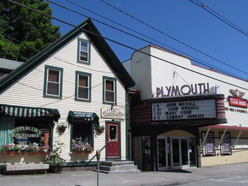 A quaint building with flower boxes beside a theater marquee listing upcoming music events.