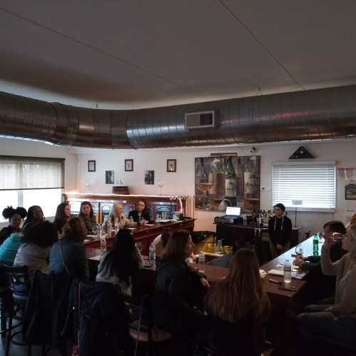 A group of people seated at a bar, engaged in conversation, with a cozy interior and soft lighting.