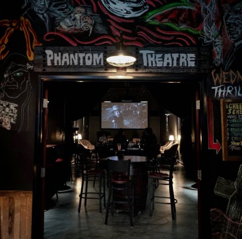Interior of Phantom Theatre with a screen showing a film, surrounded by dark walls and seating.