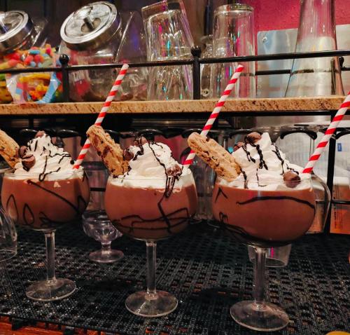 Three chocolate milkshakes topped with whipped cream, cookies, and chocolate drizzle, served in elegant glasses with striped straws.