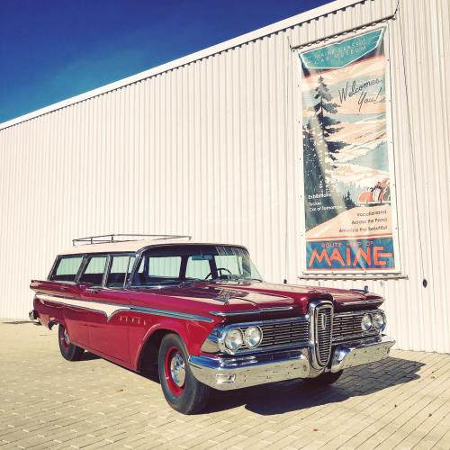 A vintage red Edsel station wagon parked in front of a building with a Maine welcome banner.