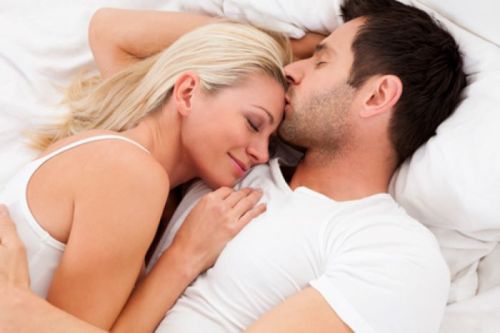A couple cuddles in bed, smiling and enjoying a moment of intimacy and affection.
