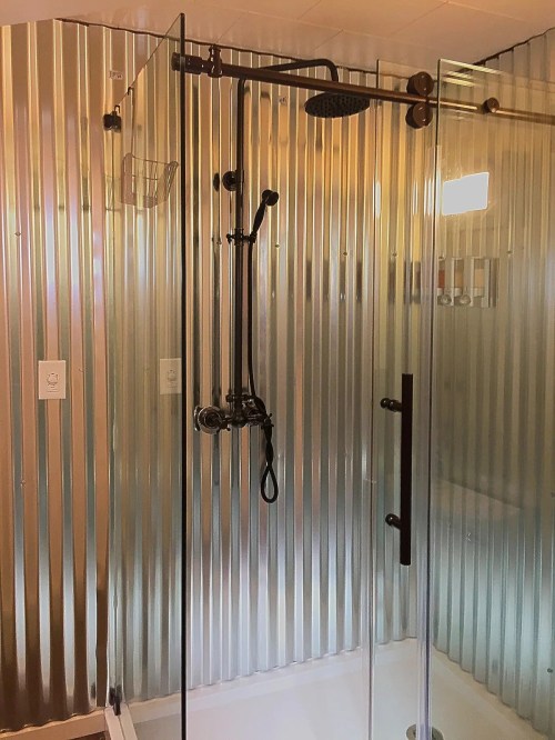 A modern shower with a glass enclosure and metal paneling, featuring a rainfall showerhead and handheld shower attachment.