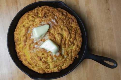 A golden-brown cornbread in a cast iron skillet, topped with two pats of melting butter.