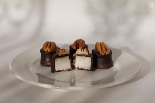 A plate of chocolate-covered candies with pecans on top, showcasing a creamy white filling inside.
