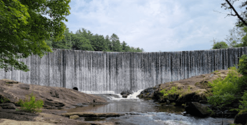 A serene waterfall cascading over a rocky ledge, surrounded by lush greenery and a calm river below.